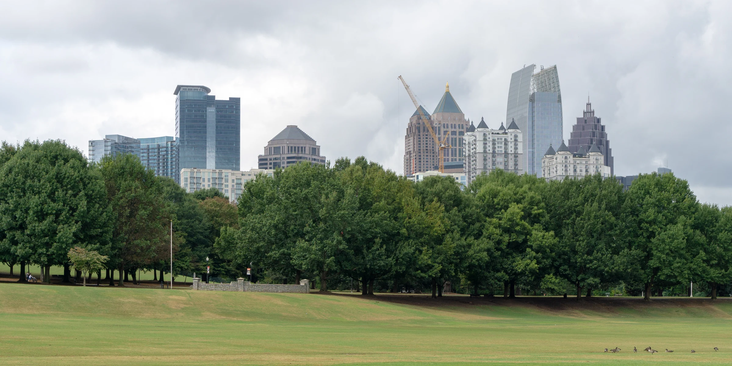 Midtown Atlanta towers behind park trees and an open lawn beneath grey clouds