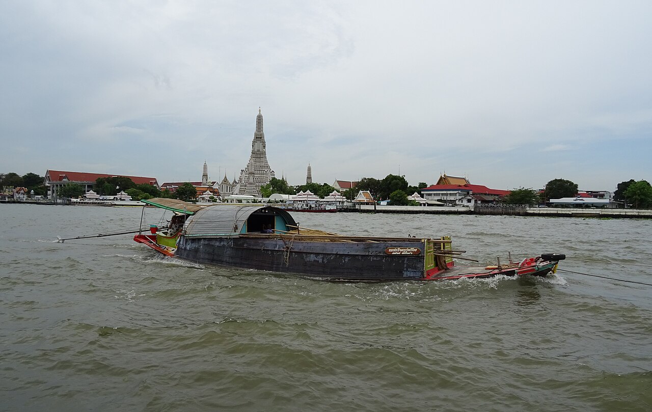 A working boat on the Chao Phraya River with Wat Arun's central tower across the water