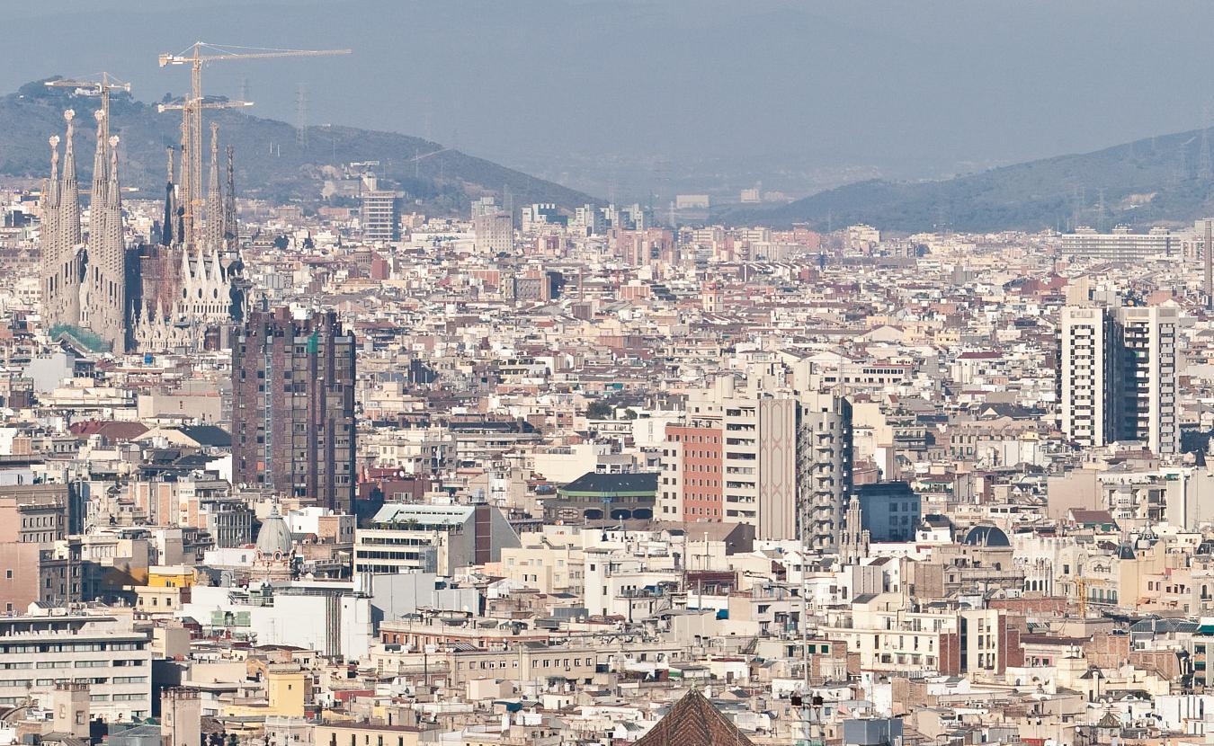 Barcelona rooftops with the towers and construction cranes of the Sagrada Família to the left and hills beyond