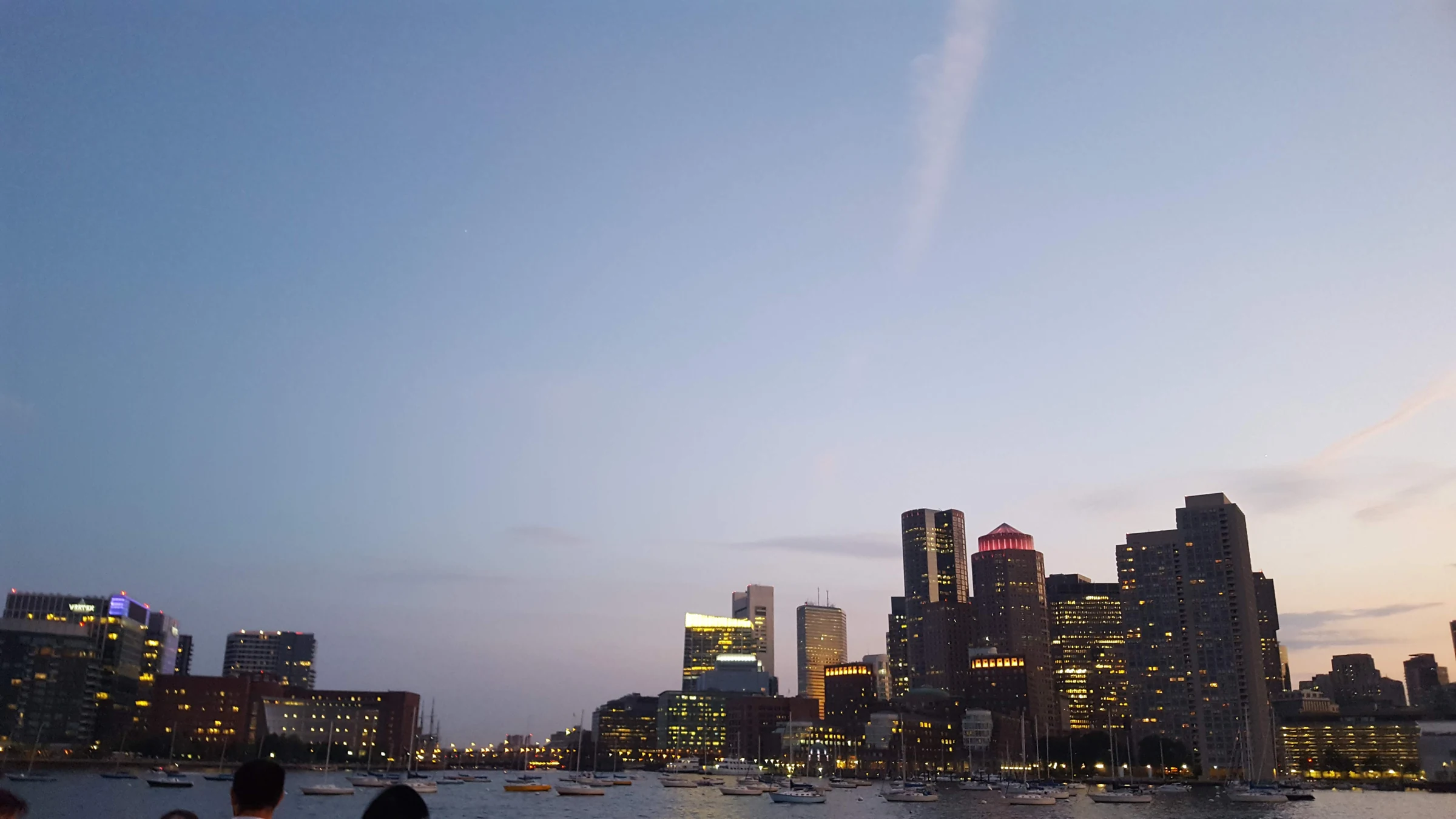 Boston harbor skyline at dusk with boats on the water