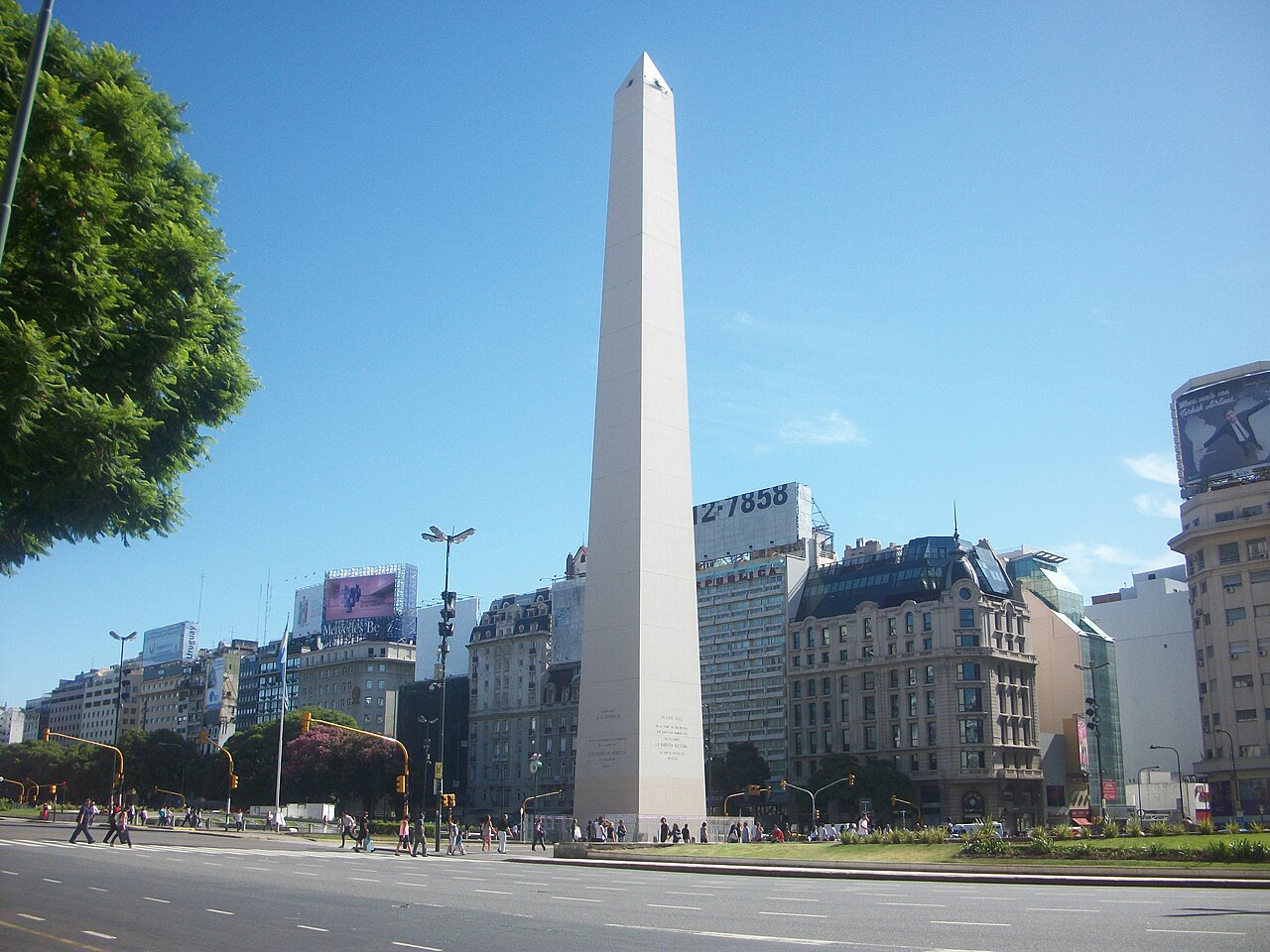 The white Obelisco in Buenos Aires beside Avenida 9 de Julio, with city buildings under a blue sky