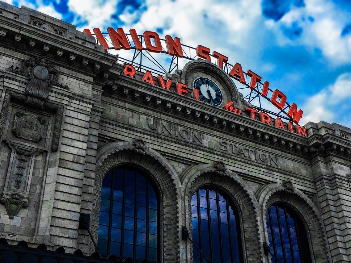 Stone arches and dark windows beneath the red Union Station sign and clock, against blue sky and white clouds
