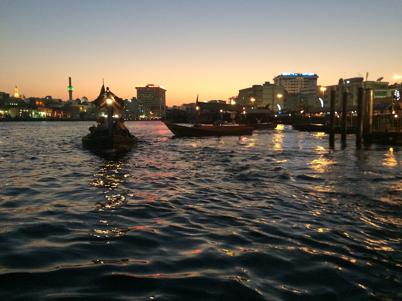 Small boats on Dubai Creek at dusk with waterfront buildings in the background