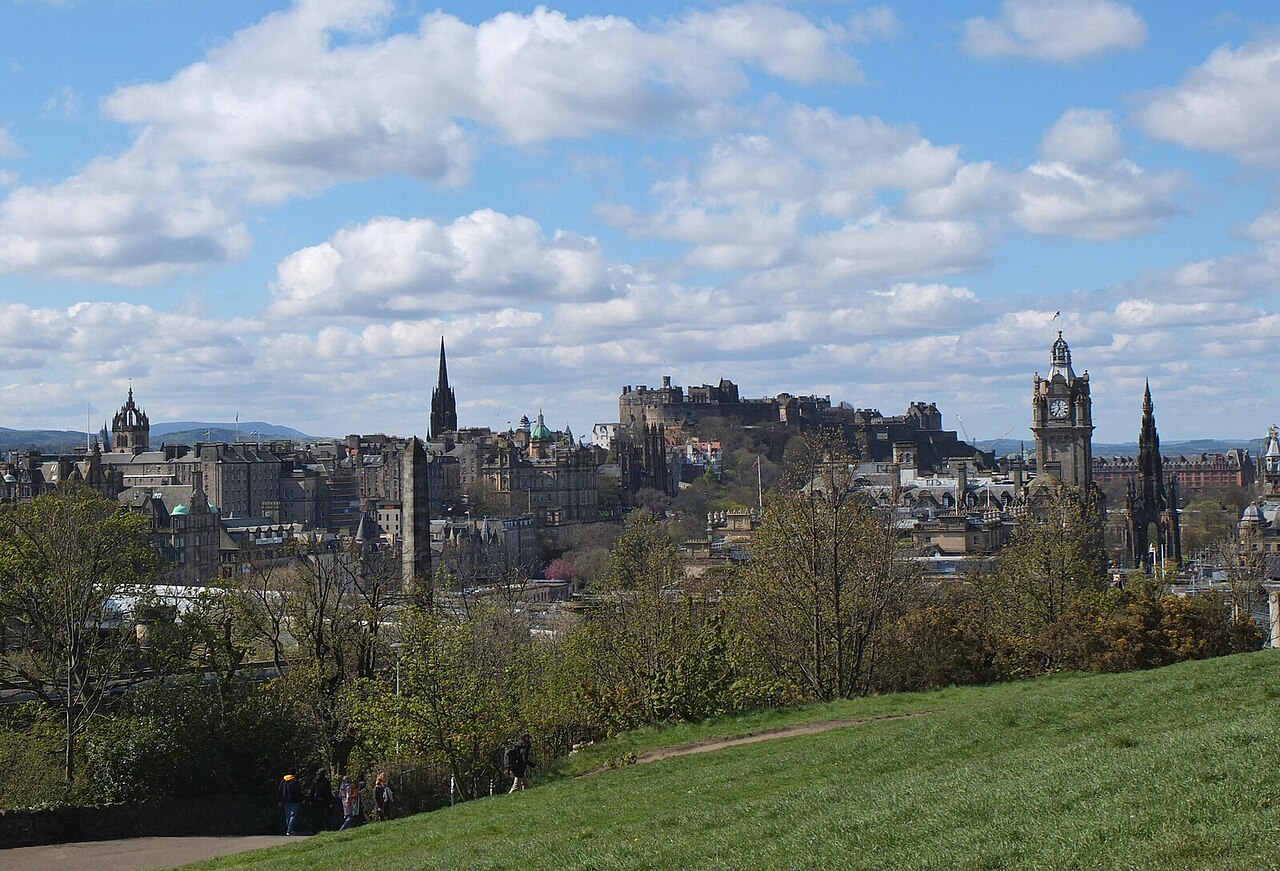 Edinburgh's skyline and castle seen from Calton Hill above trees and a grassy slope