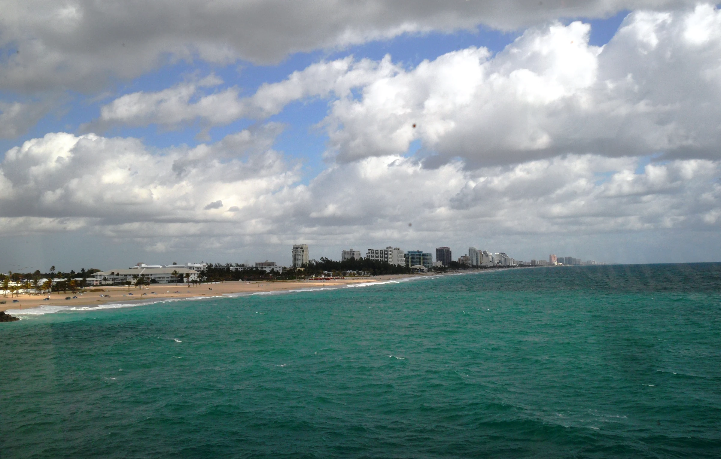 Fort Lauderdale coast with sand, buildings and turquoise water beneath large clouds