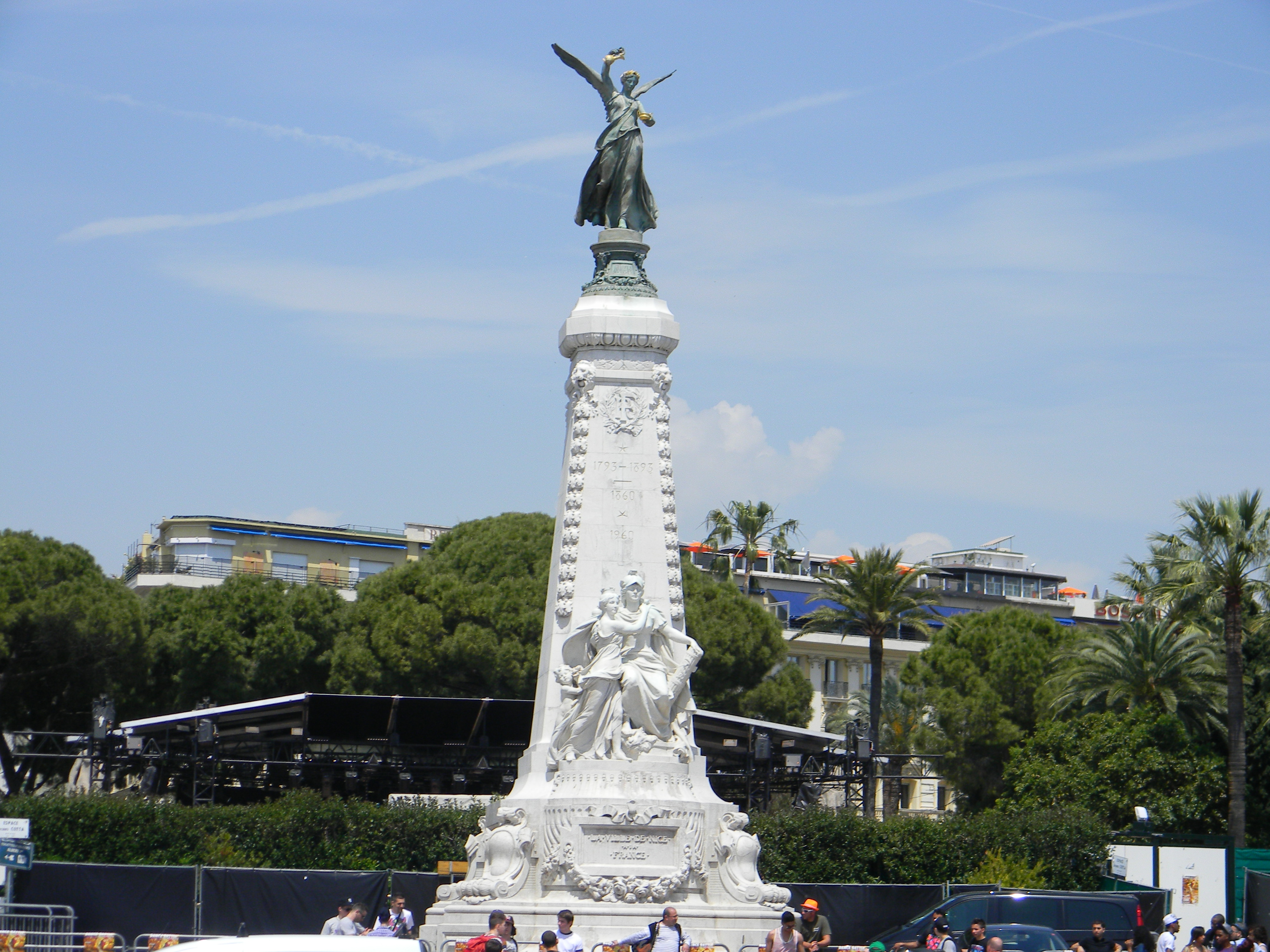 A white stone monument topped with a winged figure among palms in Nice