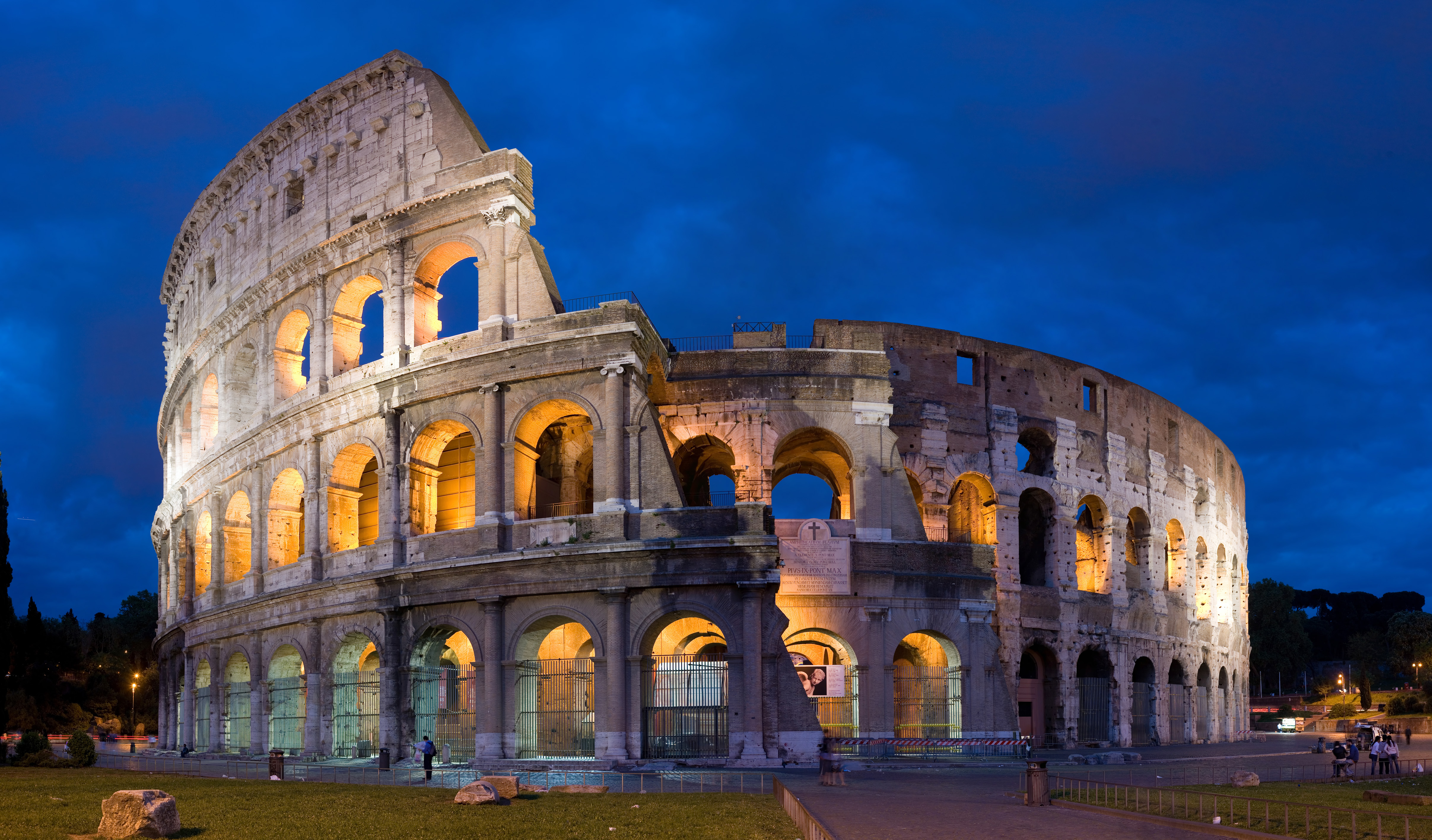 The illuminated stone arches of Rome’s Colosseum beneath a deep blue evening sky