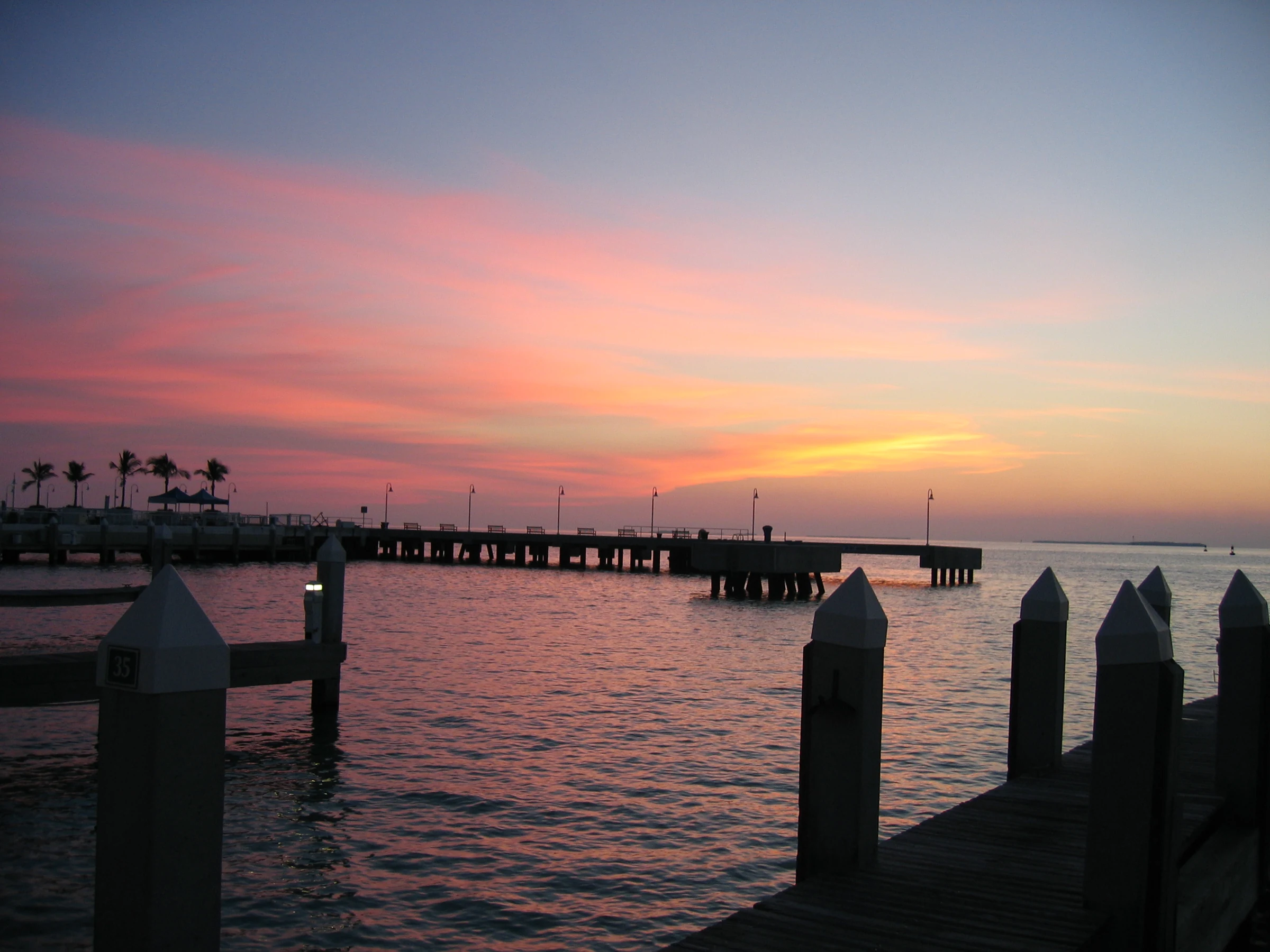 Key West waterfront at sunset with a pier, palm silhouettes and dock posts in the foreground