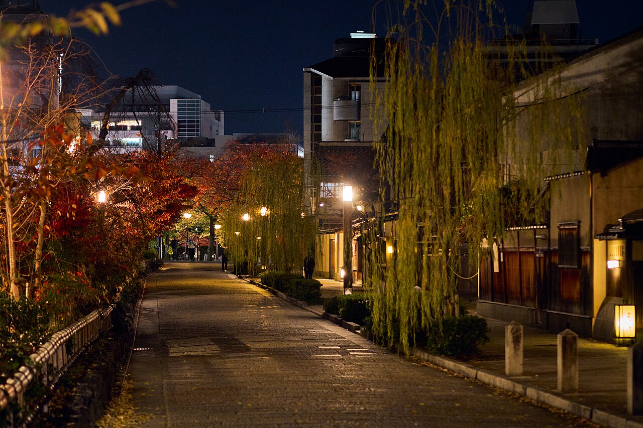 Stone-paved Gion street at night with willow trees and traditional wooden townhouses