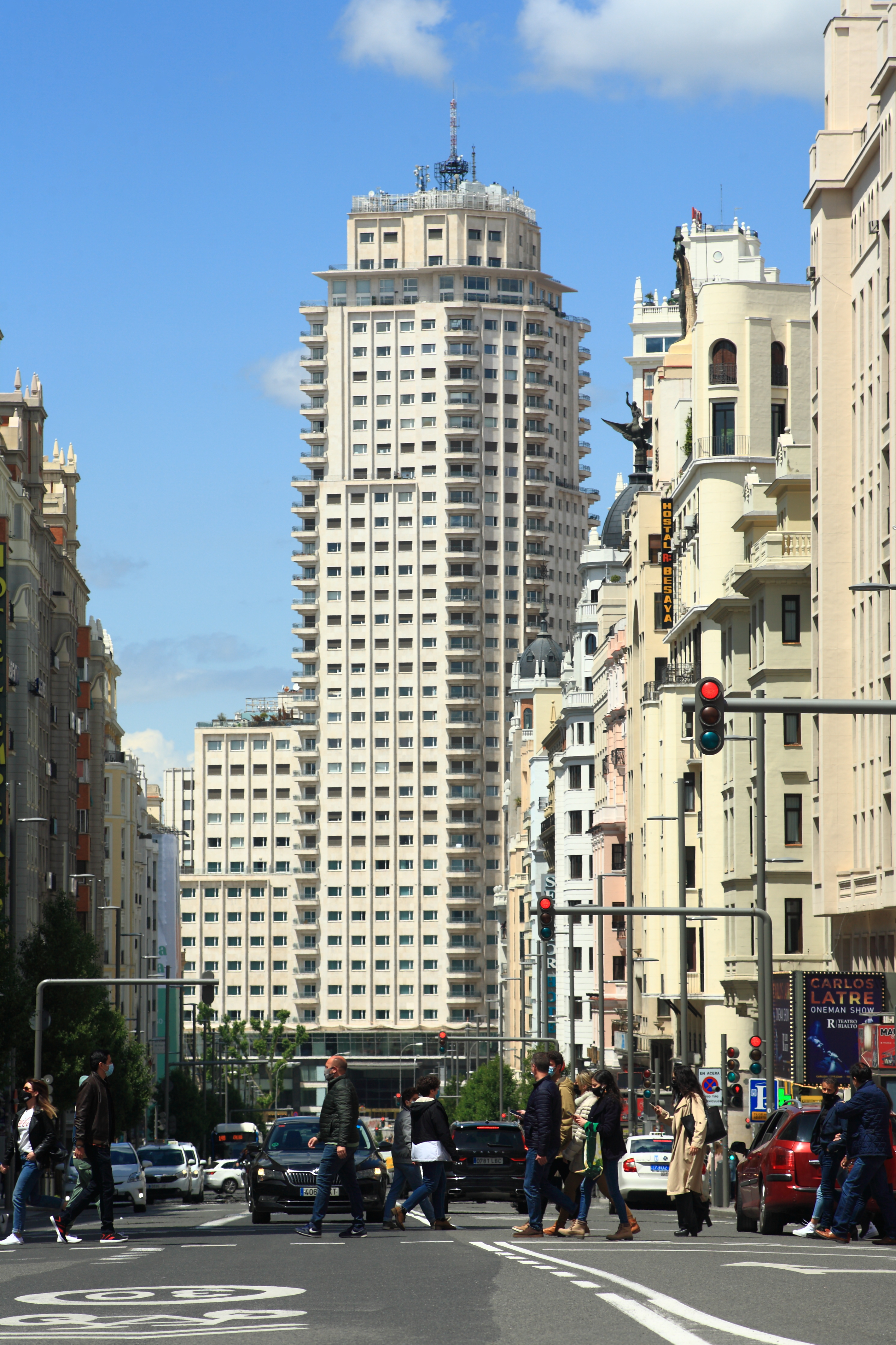 Gran Vía buildings with Torre de Madrid beyond, with traffic and people crossing the road under a blue sky