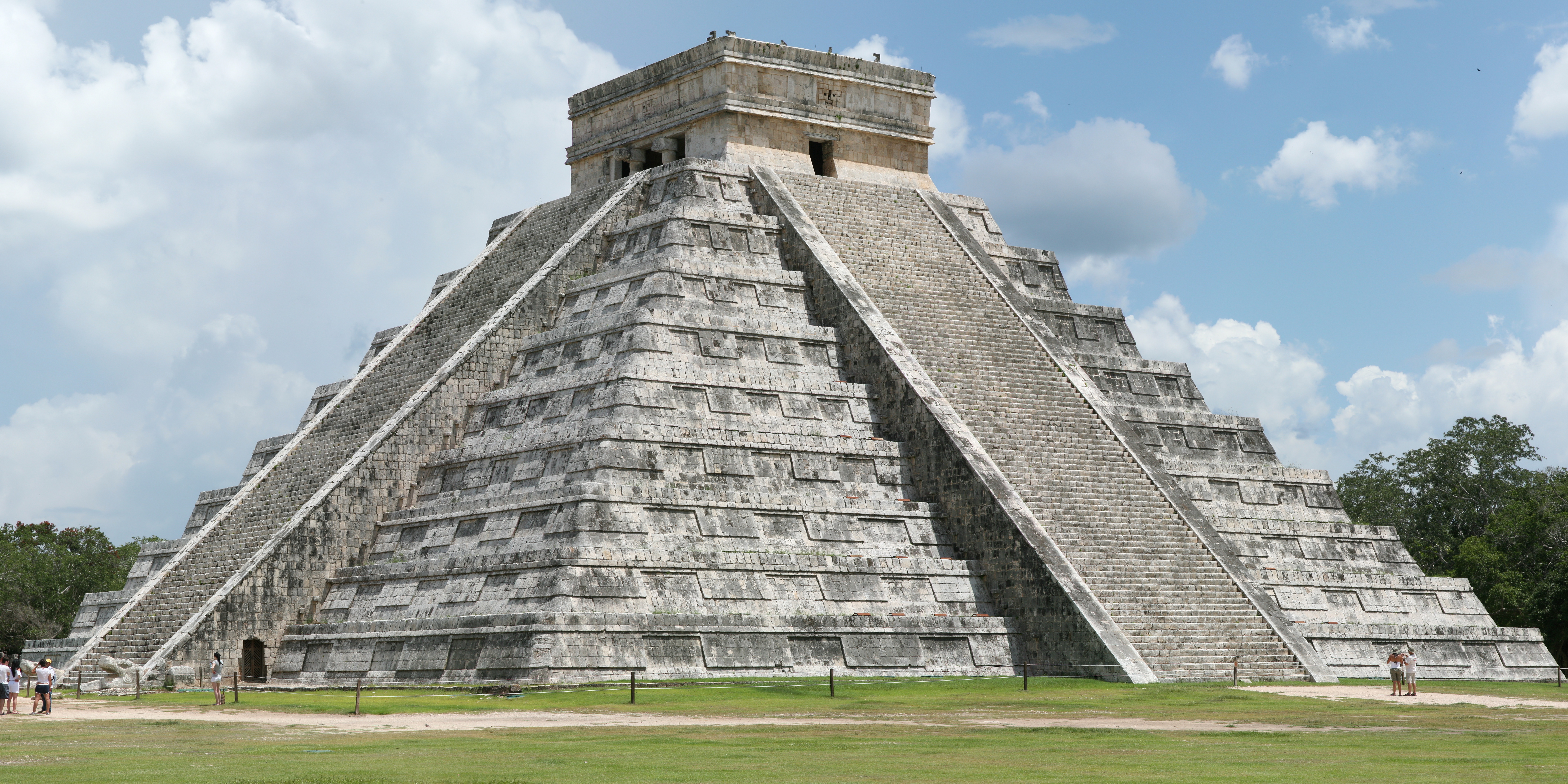 The stepped El Castillo pyramid at Chichén Itzá above a green lawn beneath a blue sky