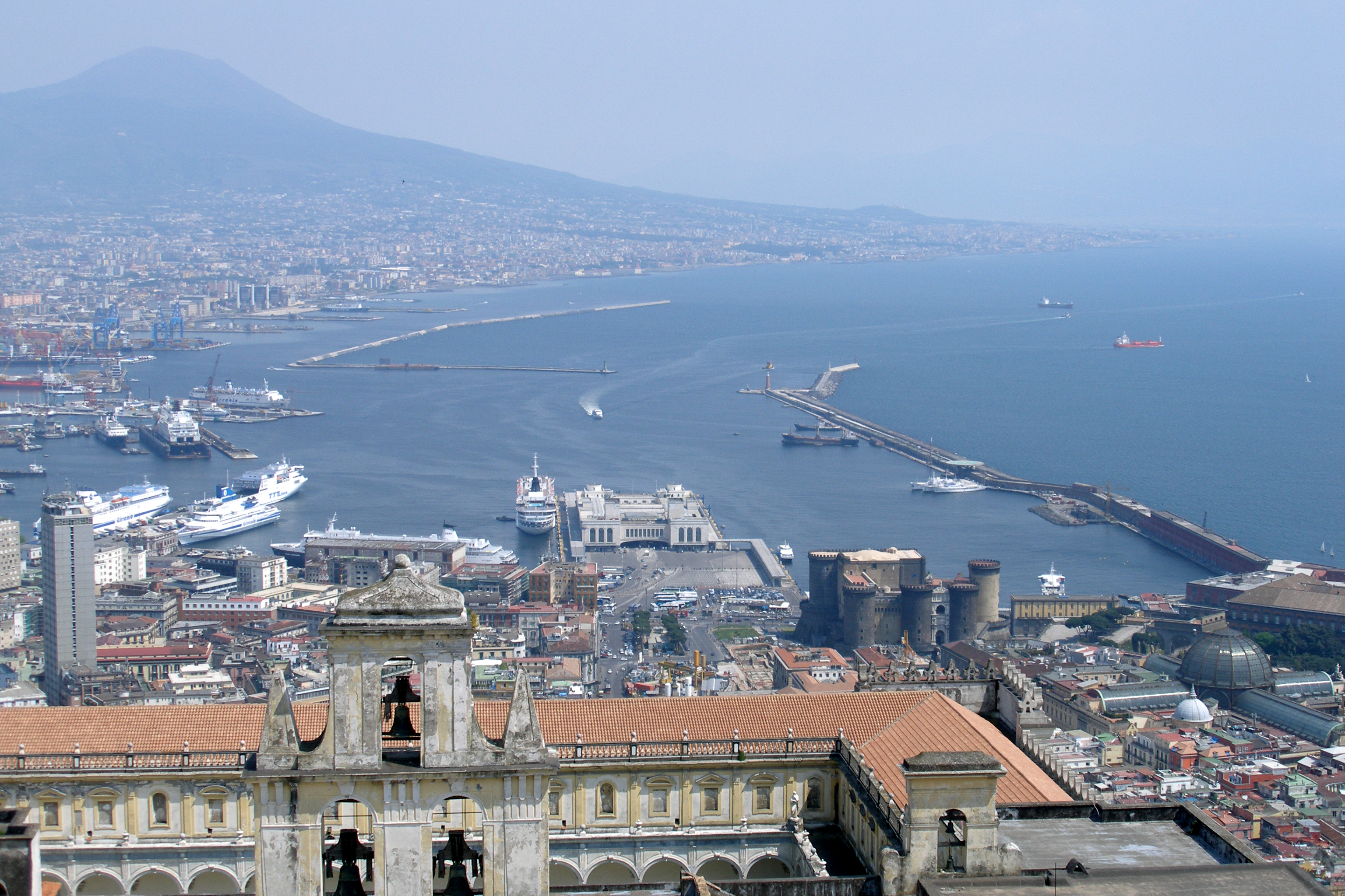 Naples port and bay below hillside buildings, with Vesuvius in the hazy distance