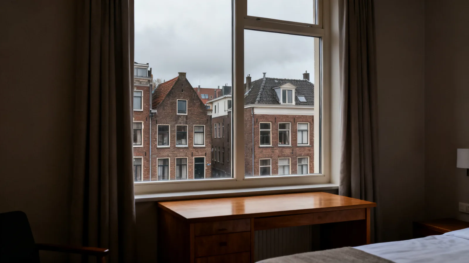 A small suitcase beside a bright hotel window and a wooden desk