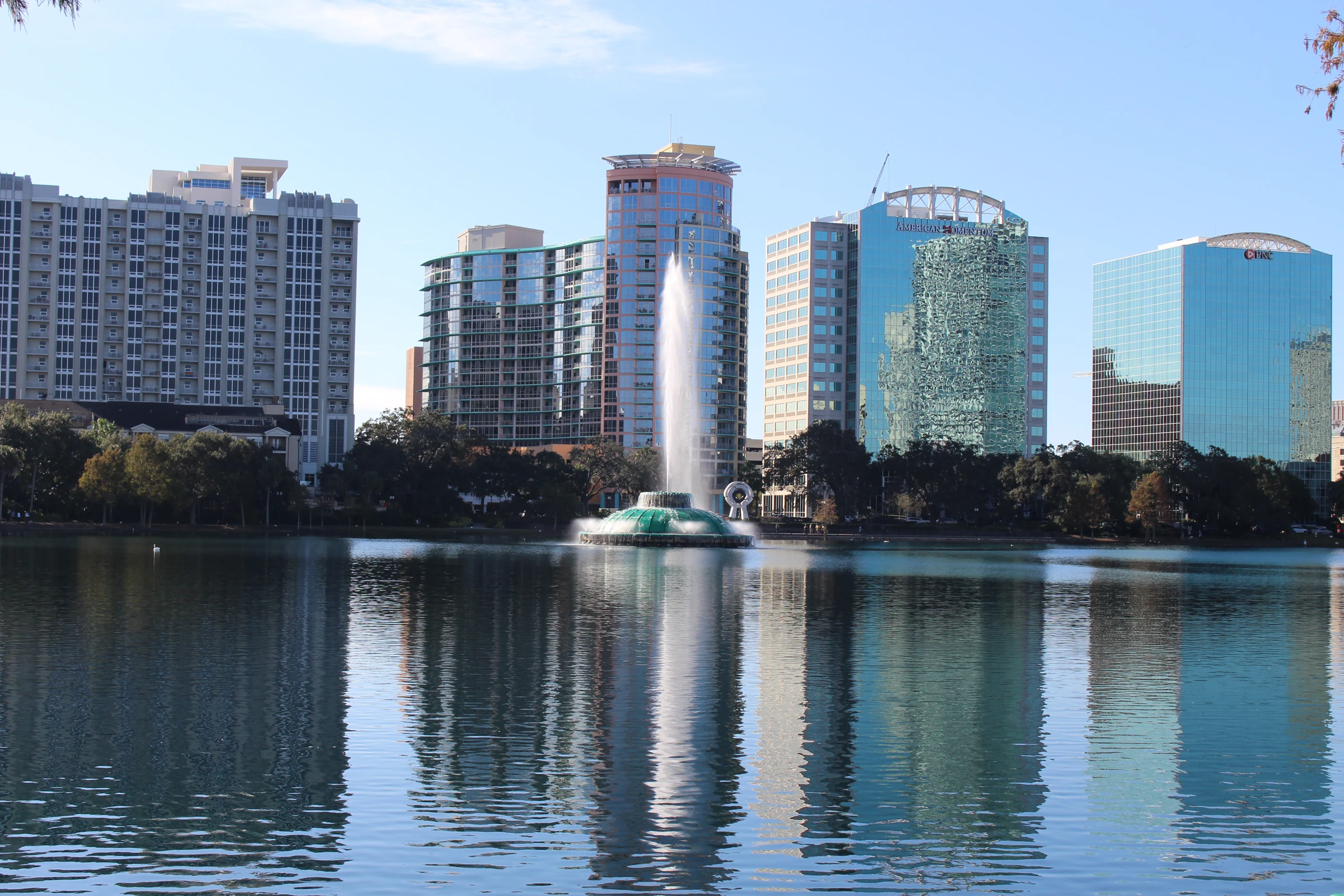 Lake Eola fountain and Downtown Orlando towers reflected in the water beneath a blue sky