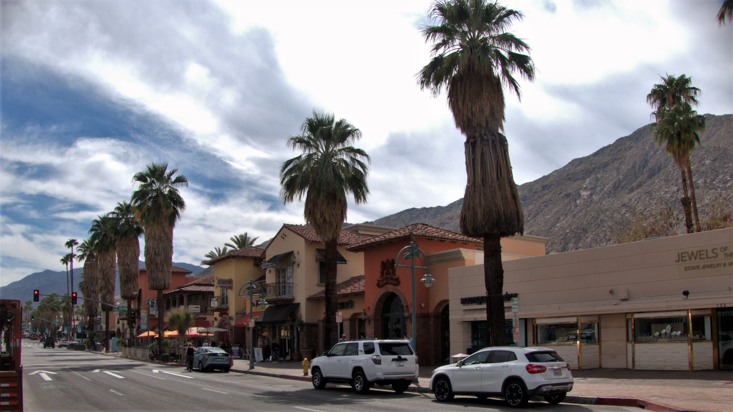 Palm Canyon Drive in Downtown Palm Springs with palms, low-rise shops and mountains beneath clouds