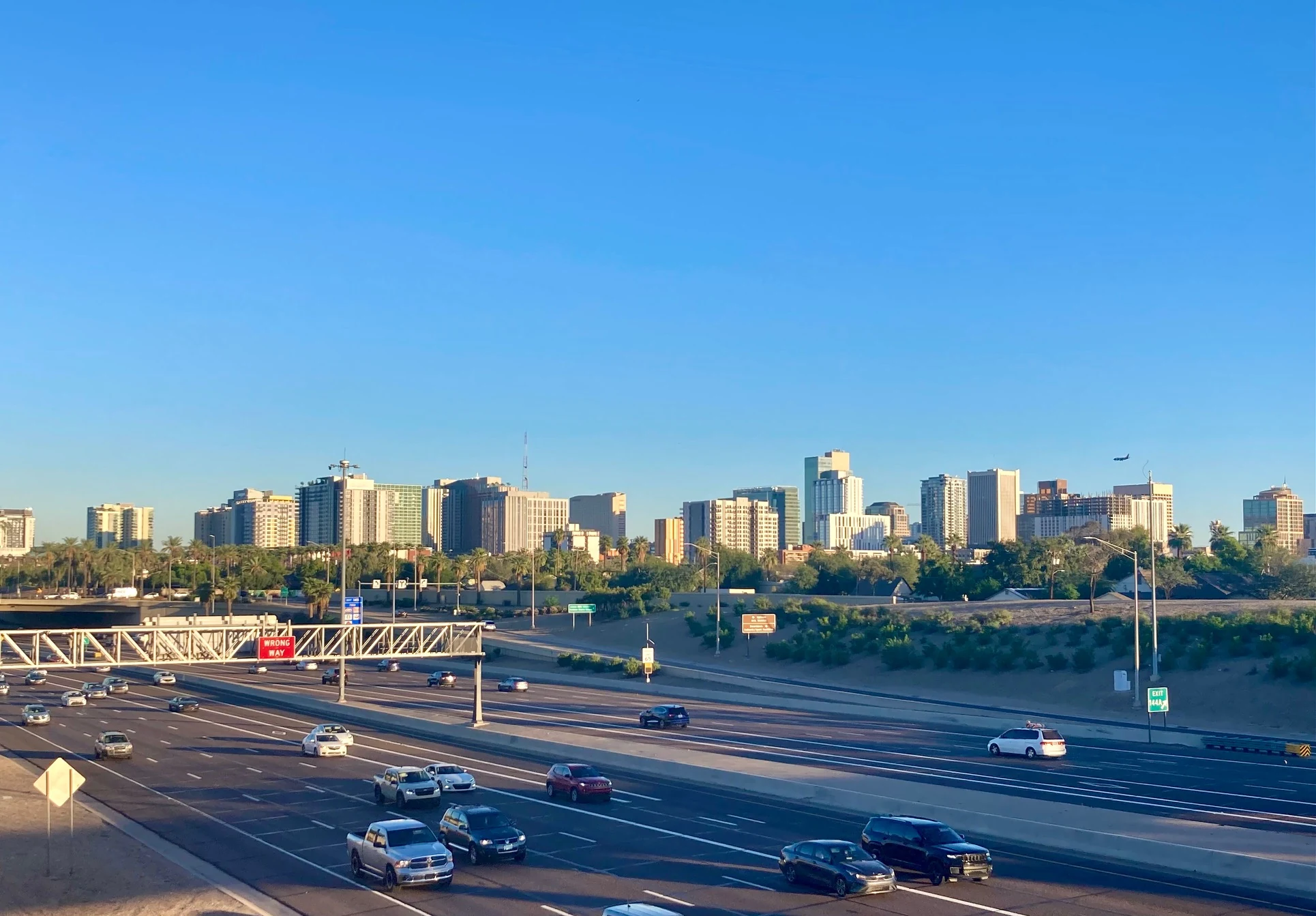 Downtown Phoenix skyline beyond a multilane road with palms, low-rise buildings and blue sky