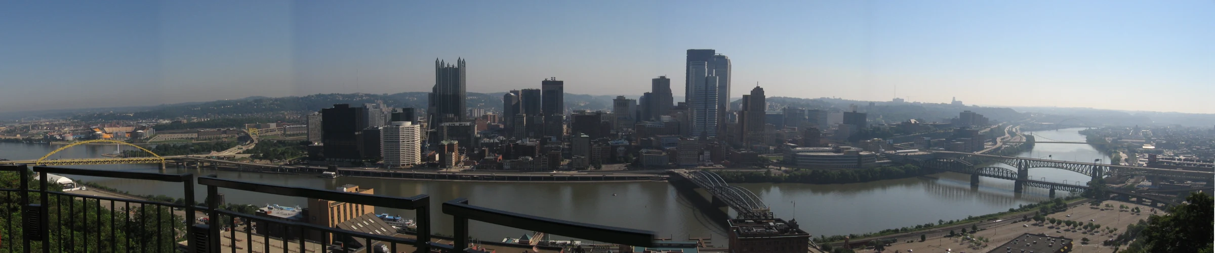 Historical panorama of Downtown Pittsburgh across the river, with bridges and a viewing-deck rail in front