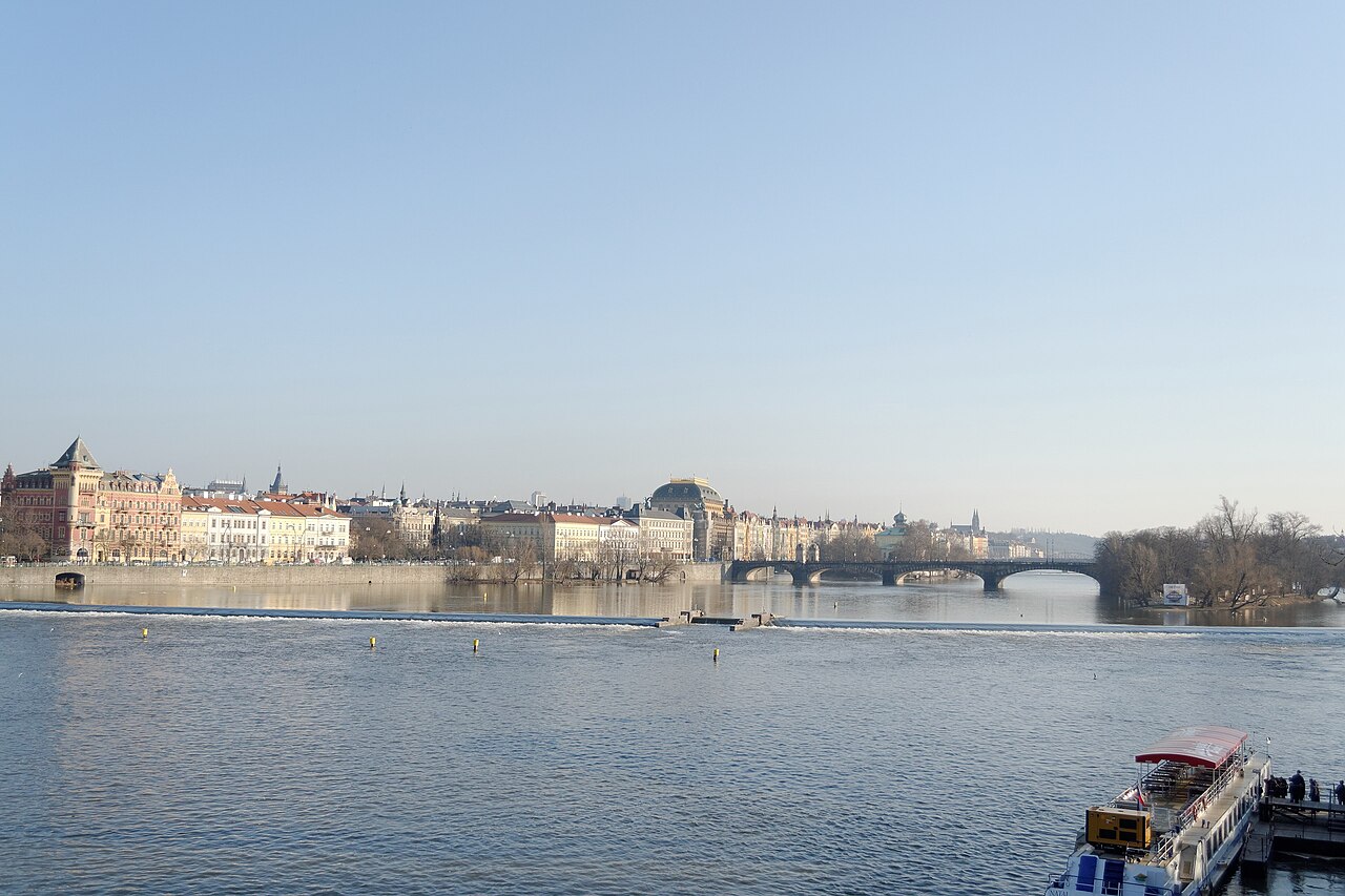 The Vltava river in Prague with riverside buildings, a distant bridge and a moored boat