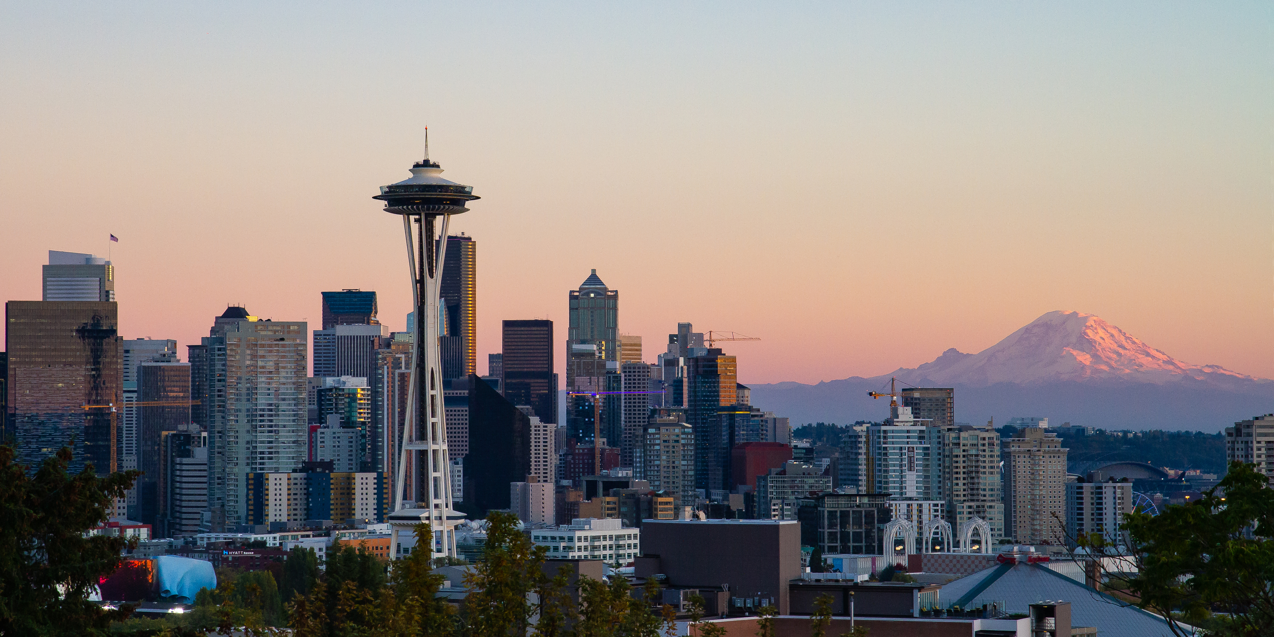 Seattle skyline with the Space Needle left of center and Mount Rainier at right under a peach evening sky
