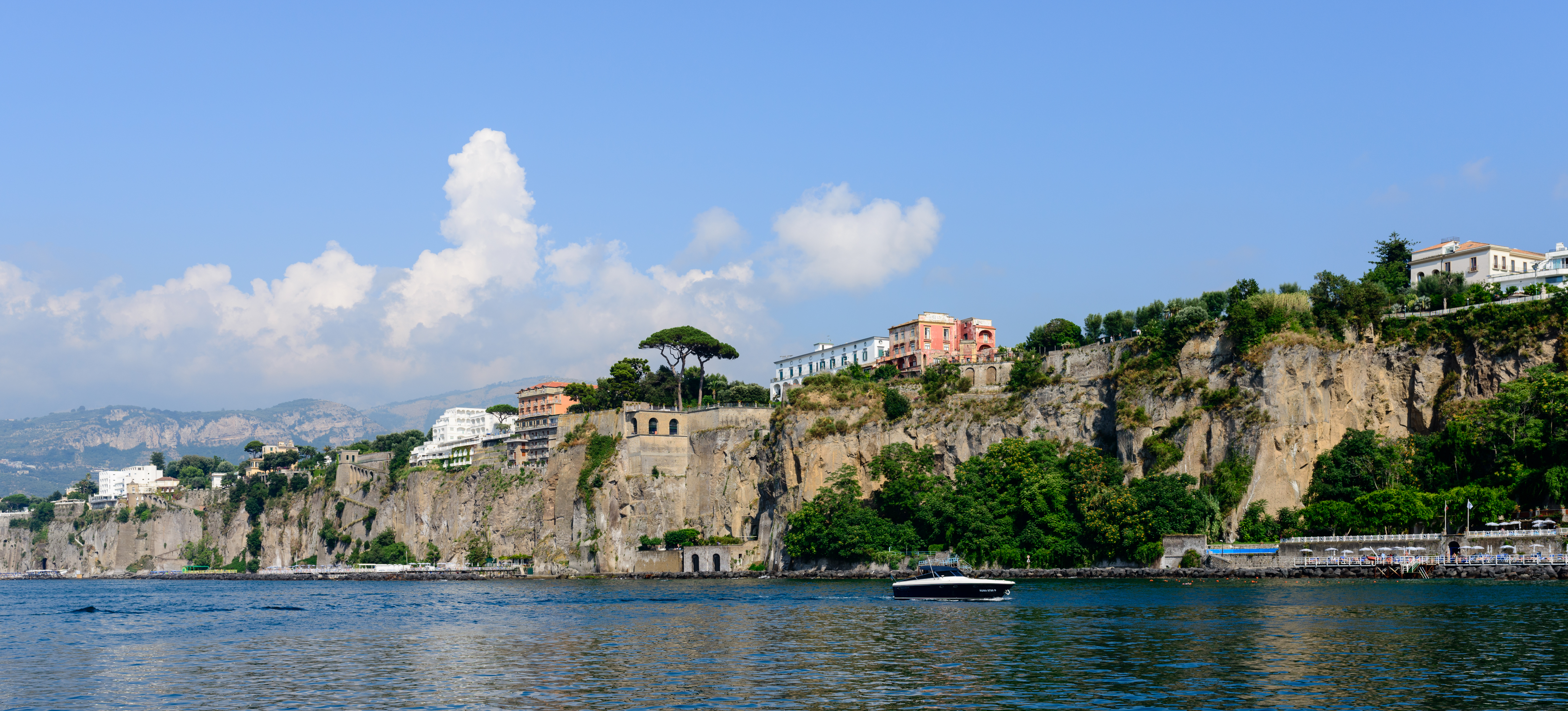 Sorrento coastal cliffs with buildings above the rock face and a boat on the blue water