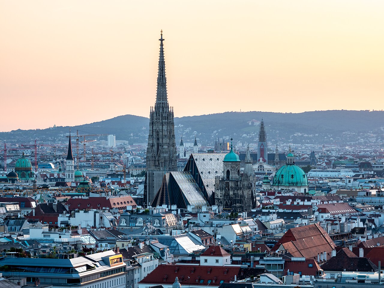 Vienna's Stephansdom tower and patterned cathedral roof above city rooftops in warm evening light