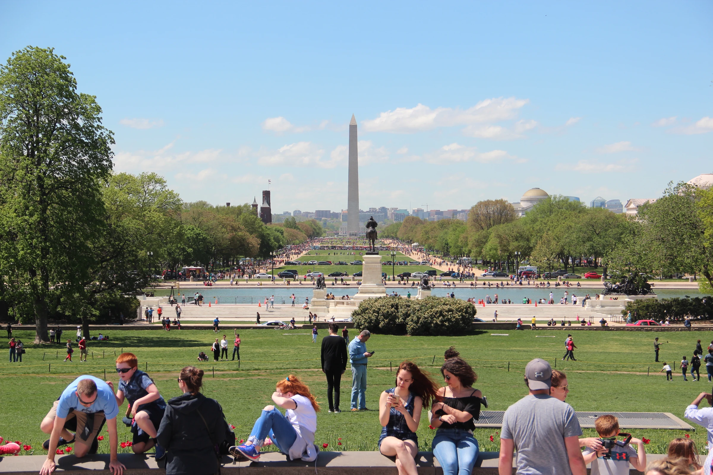 National Mall lawn and paths viewed west from the Capitol toward the Washington Monument beneath blue sky with scattered clouds